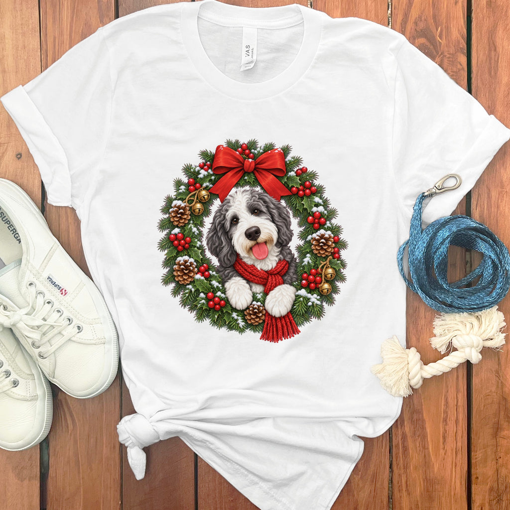 White crewneck t-shirt featuring a doodle dog wearing a red scarf inside a Christmas wreath.