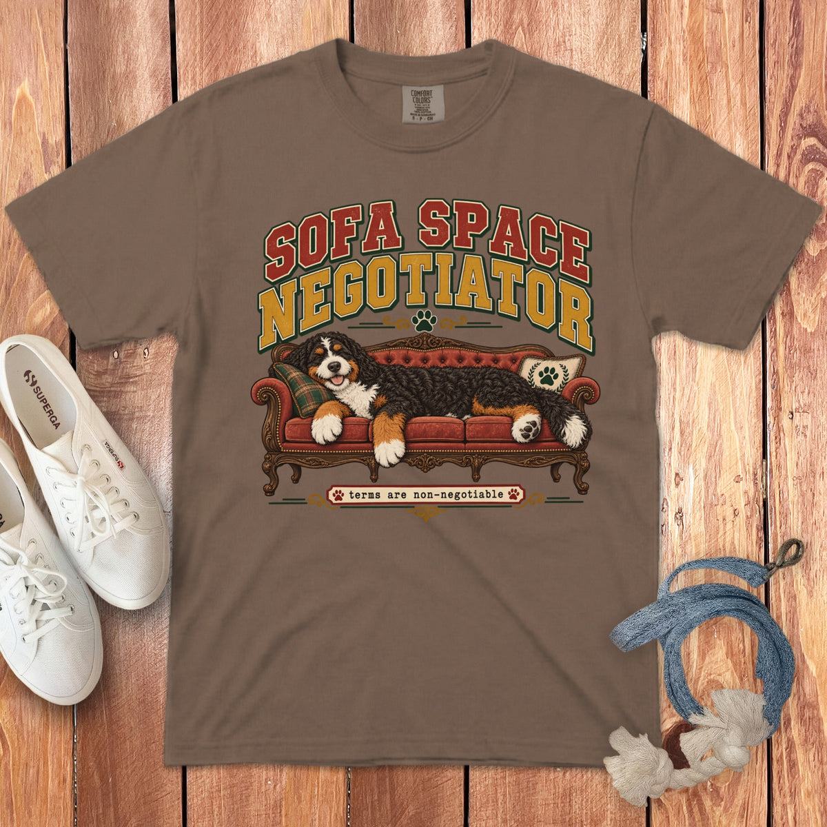 Brown t-shirt featuring a graphic of a Bernese Mountain Dog lying on a red couch, with the text "Sofa Space Negotiator."