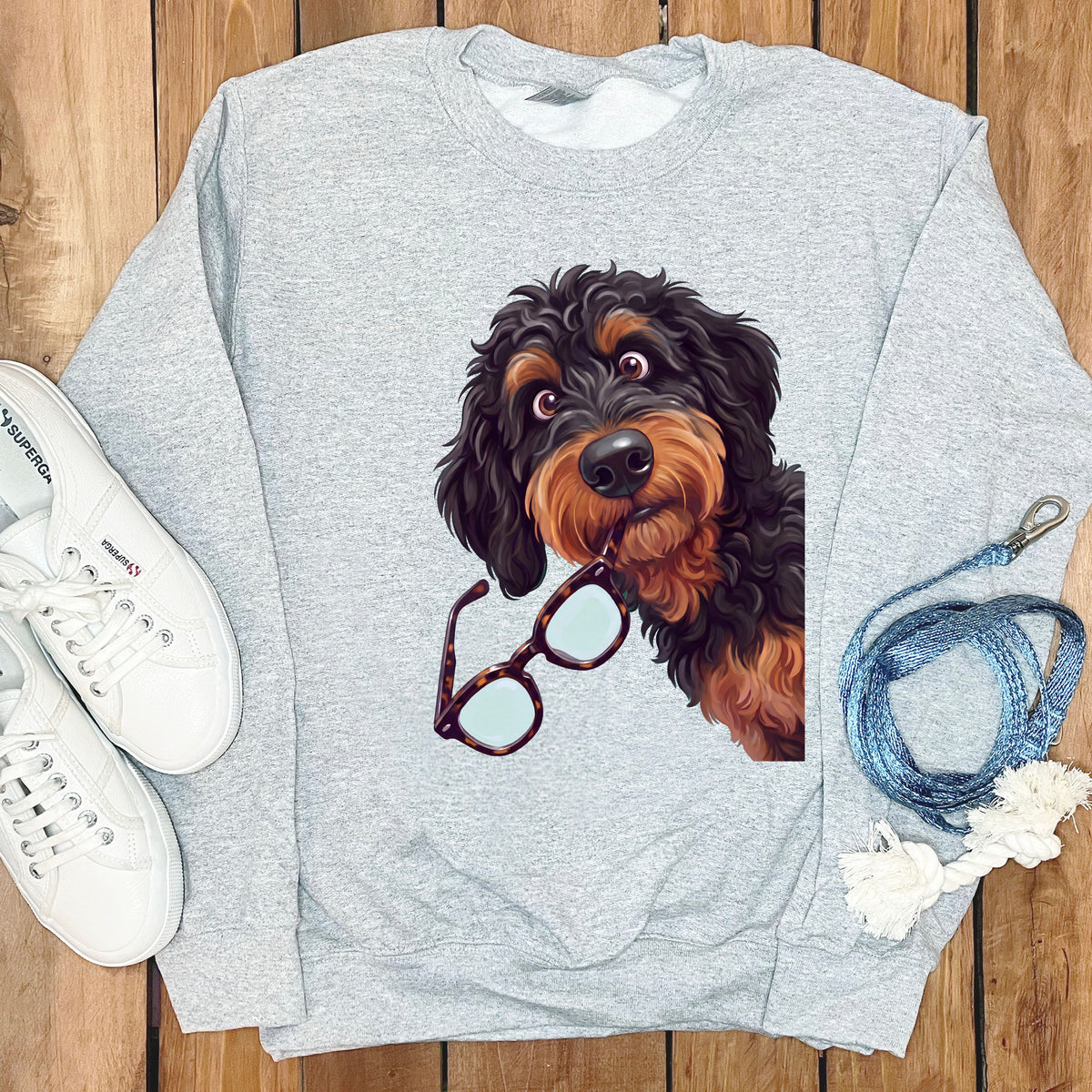 Gray crewneck sweatshirt featuring a graphic of a black and tan doodle dog holding glasses in its mouth.