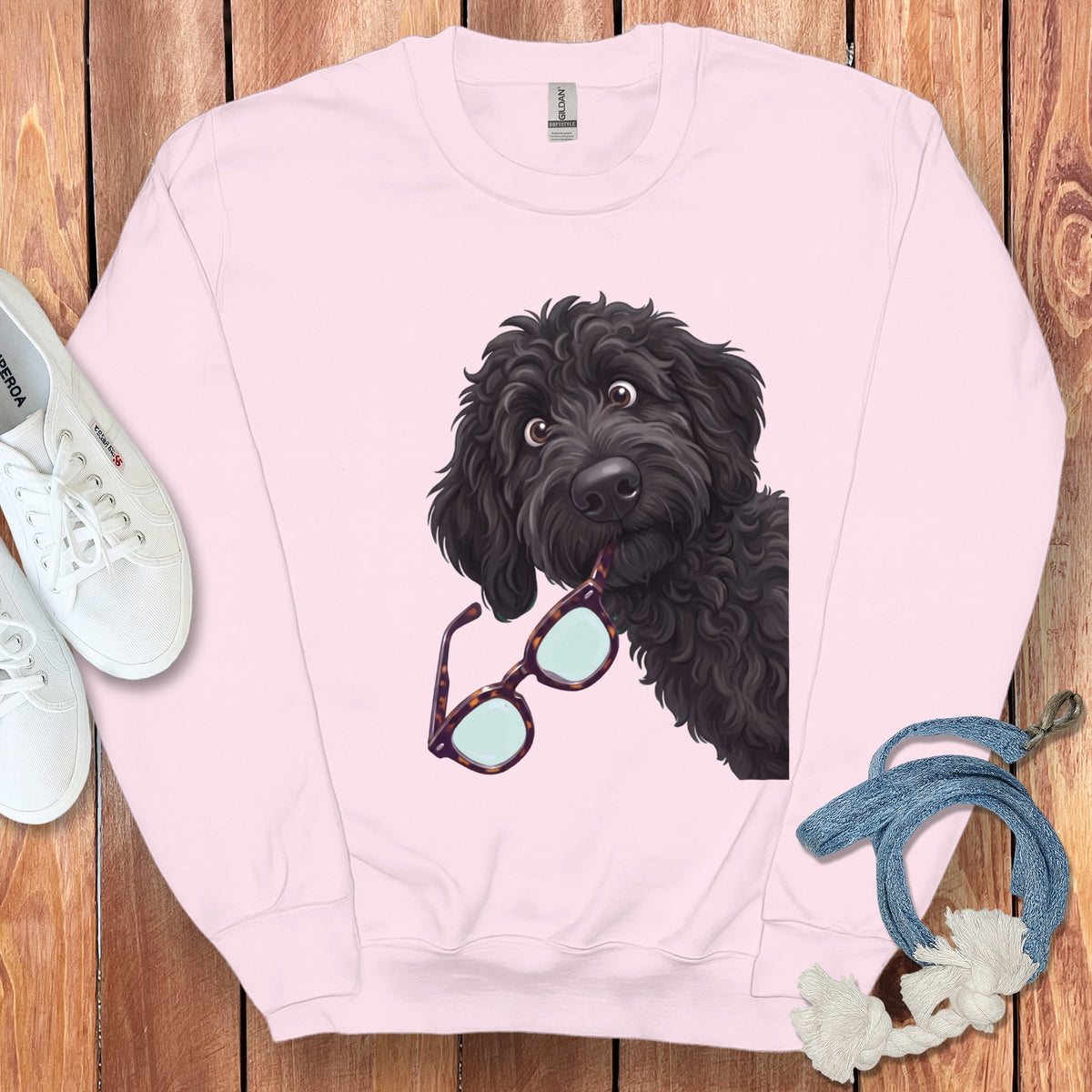 A light pink crewneck sweatshirt features an illustration of a black poodle holding glasses in its mouth.