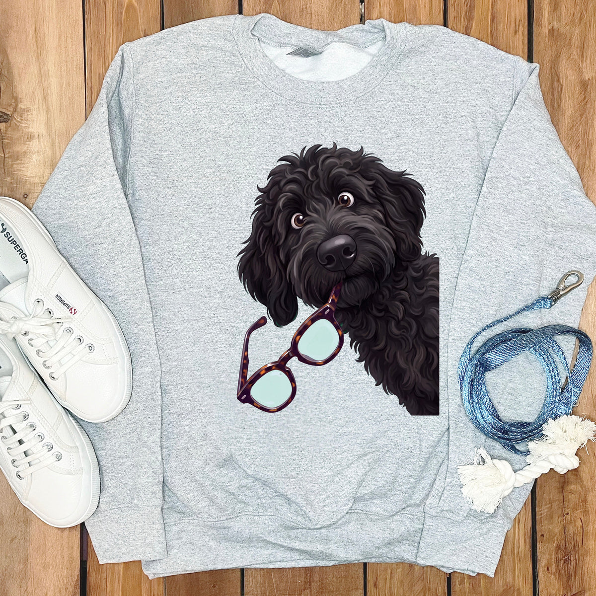 A gray crewneck sweatshirt featuring a graphic of a black poodle holding tortoise-shell glasses in its mouth.