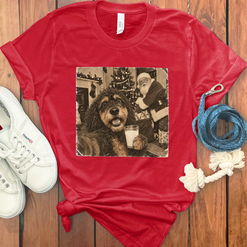 A red t-shirt printed with a vintage black-and-white photo of a dog holding a glass of milk near Santa Claus.