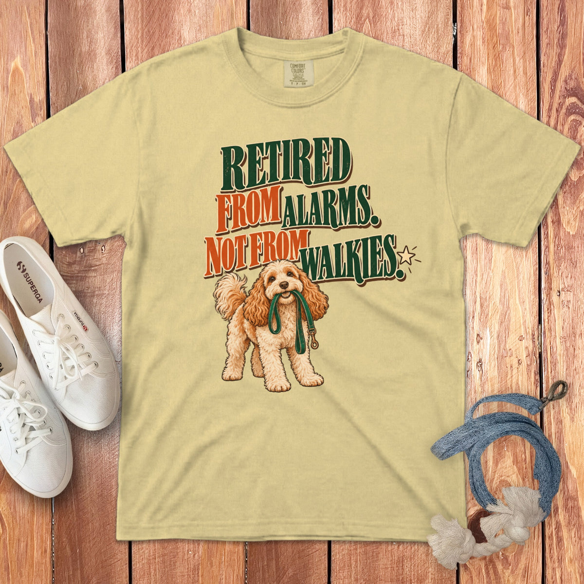 A cream t-shirt with the text Retired From Alarms, Not From Walkies above an illustration of a dog holding a leash.