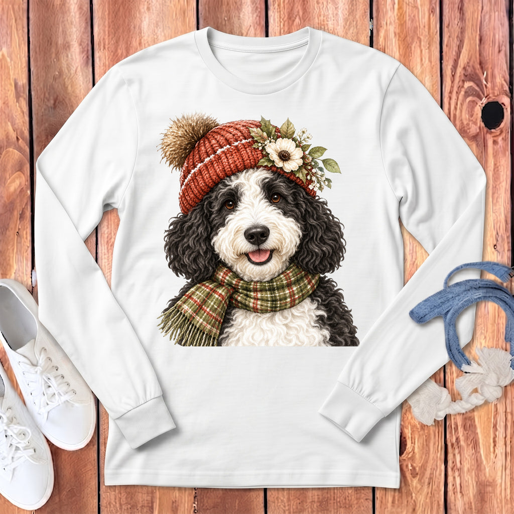 Bernedoodle dog wearing a red knitted hat and plaid scarf on a white long-sleeve shirt.