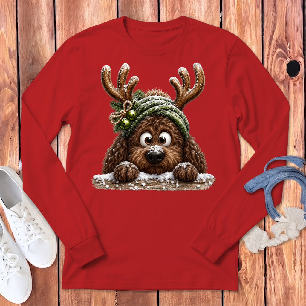 Brown dog with antlers and festive hat peeking over a snowy wooden fence.