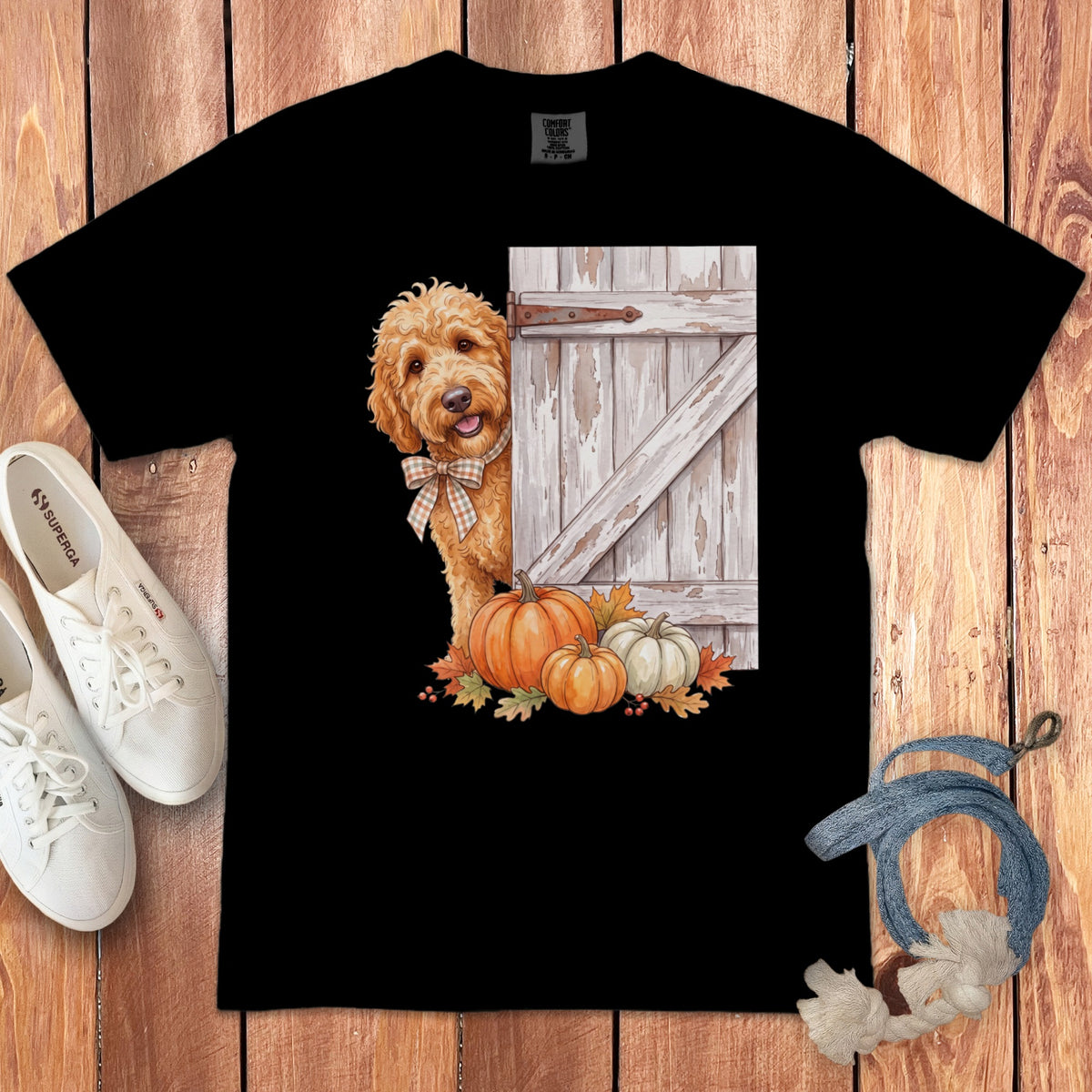 Black t-shirt with a watercolor print of a golden doodle peeking from behind a barn door with pumpkins.