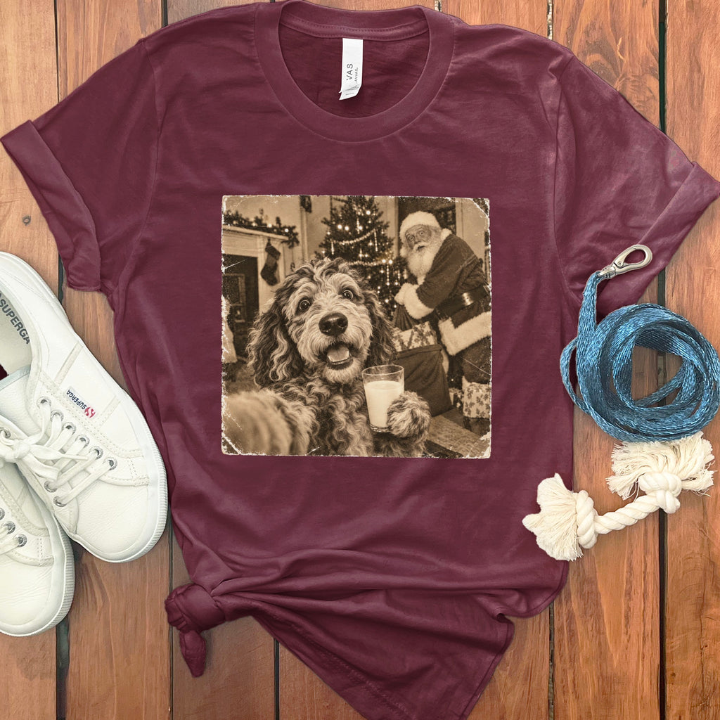 Maroon t-shirt featuring a graphic of a dog holding a glass of milk with Santa Claus in the background.