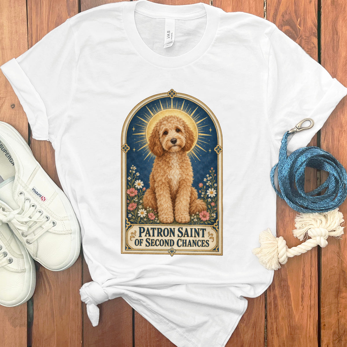 White t-shirt with a gold-framed illustration of a fluffy dog and flowers with text.