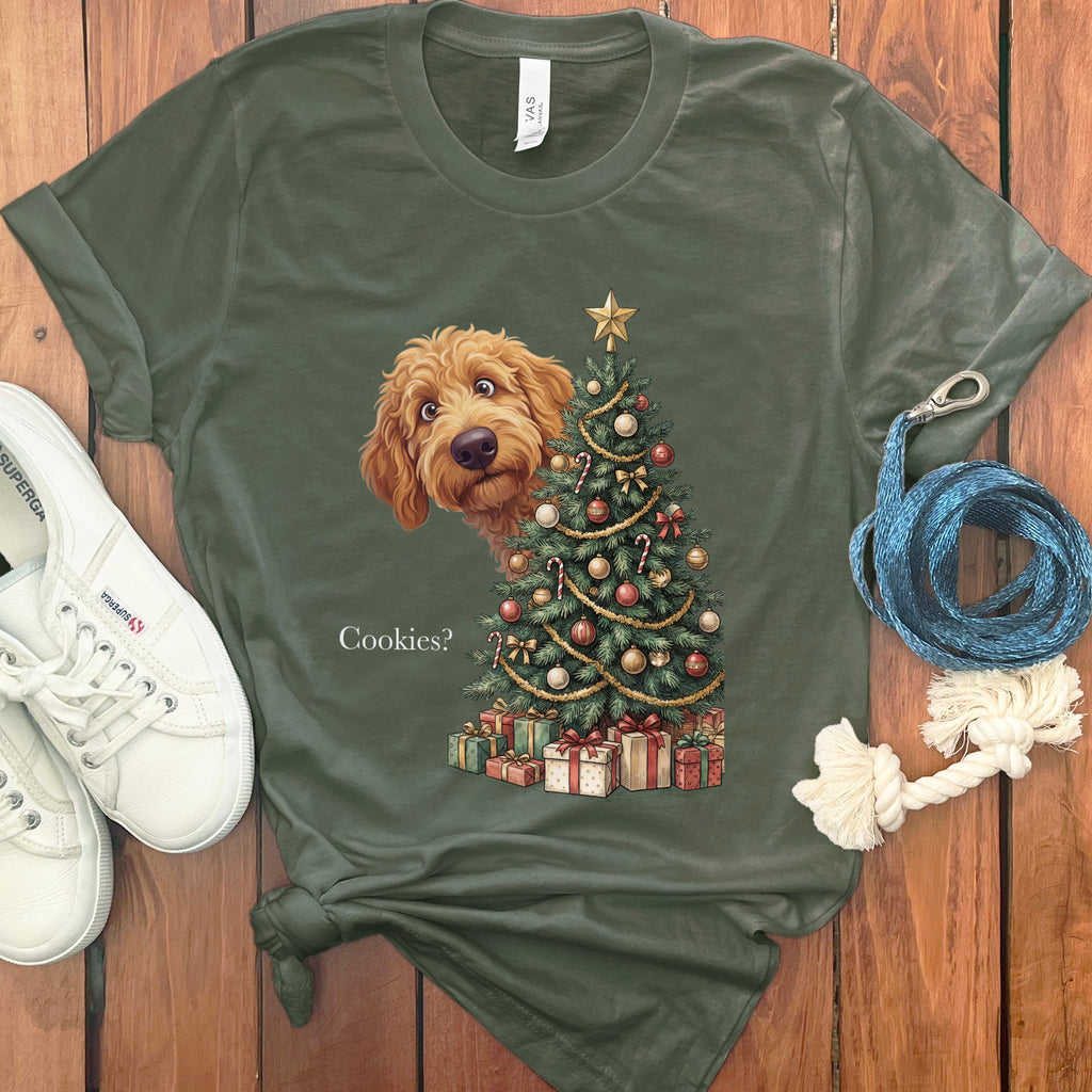 Olive green t-shirt with a doodle peeking behind a Christmas tree that asks "Cookies?".