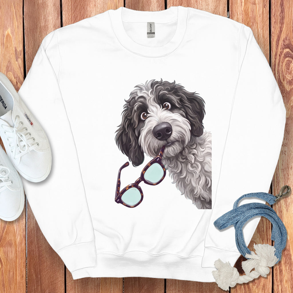 A white crewneck sweatshirt displays a graphic of a black and white doodle dog holding glasses in its mouth.