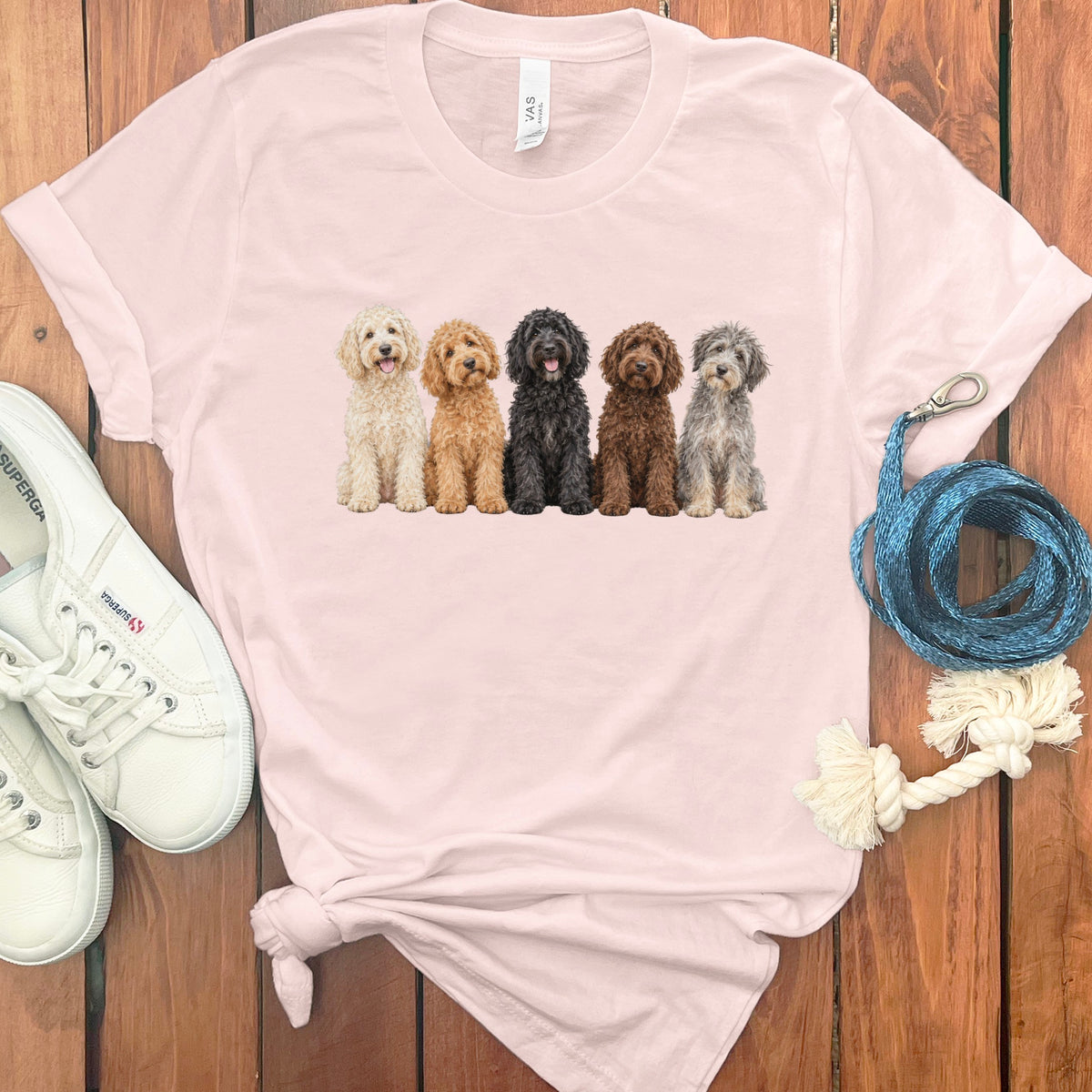 Pink t-shirt with a print of five different colored dogs sitting in a row.