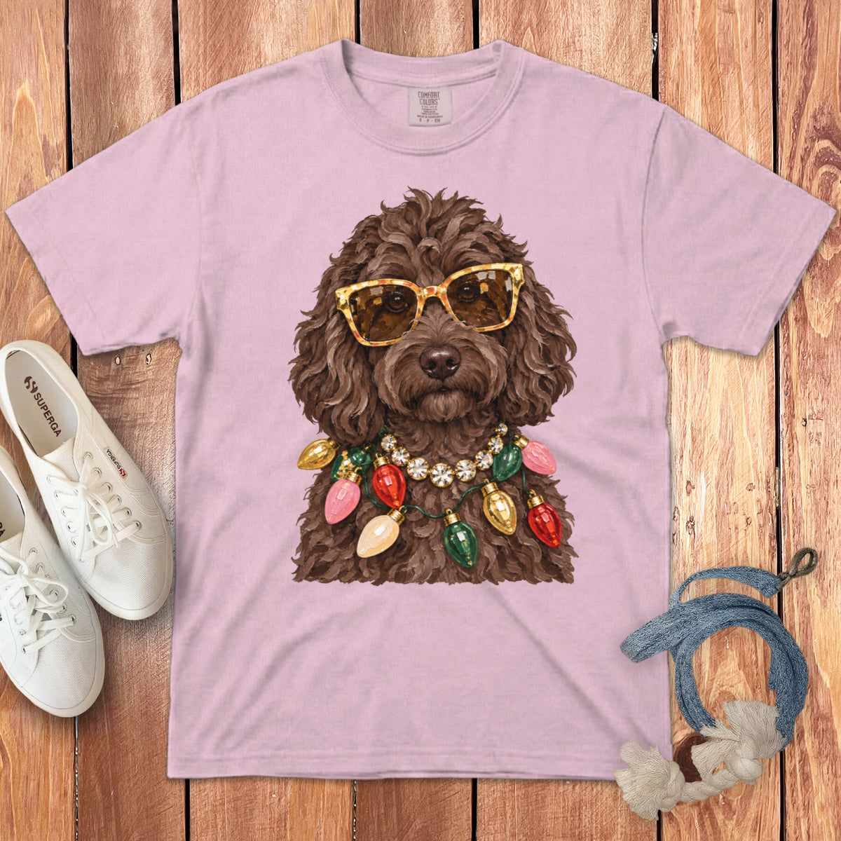 Brown dog wearing sunglasses and a Christmas light necklace on a pink t-shirt.