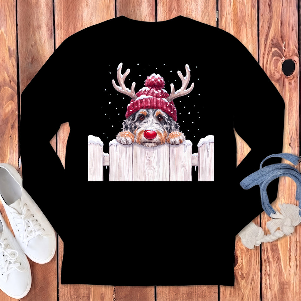 A black long-sleeve t-shirt with a graphic of a dog wearing a red beanie with reindeer antlers behind a snowy fence.