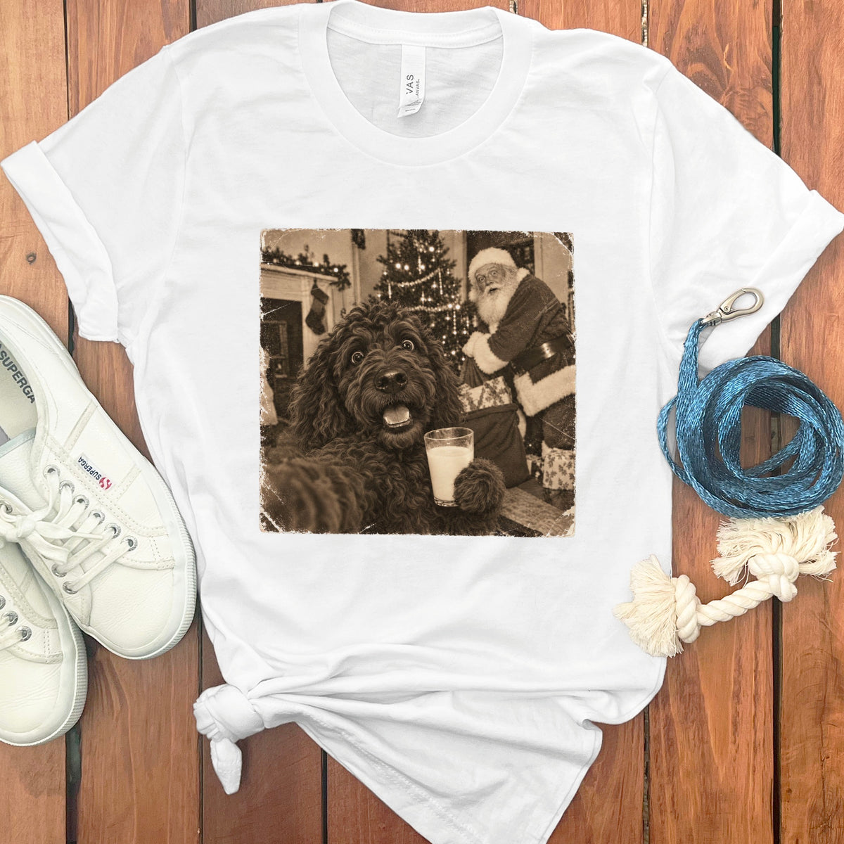 A white t-shirt featuring a vintage sepia graphic of a curly dark dog holding a glass of milk with Santa Claus in the background.