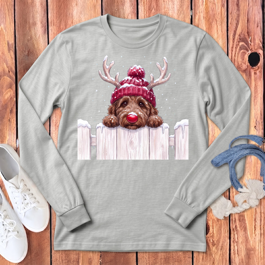 Dog wearing a red Christmas hat and reindeer antlers peeking over a snowy fence.