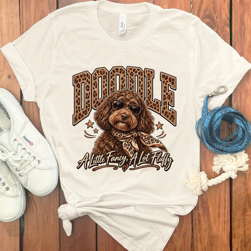 White t-shirt with "Doodle" text, a dog in sunglasses and scarf, and "A Little Fancy, A Lot Fluffy" text.