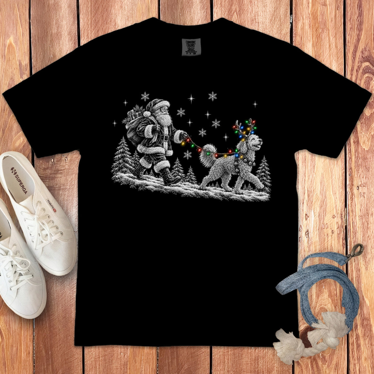 A black crewneck t-shirt featuring a vintage-style graphic of Santa Claus walking a fluffy dog wearing colorful Christmas lights on a snowy path.