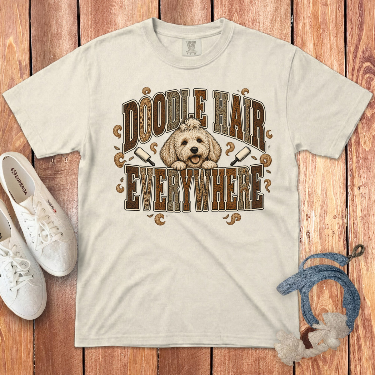 Beige t-shirt featuring a cartoon doodle dog graphic with the text Doodle Hair Everywhere on a wooden background.