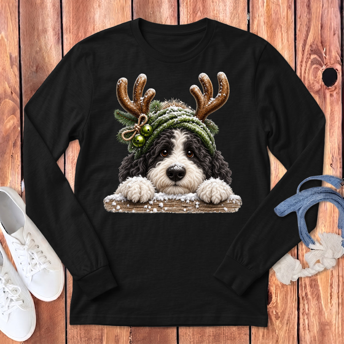 Bernedoodle dog wearing antlers and green beanie with bells and snow on a black long-sleeve shirt.