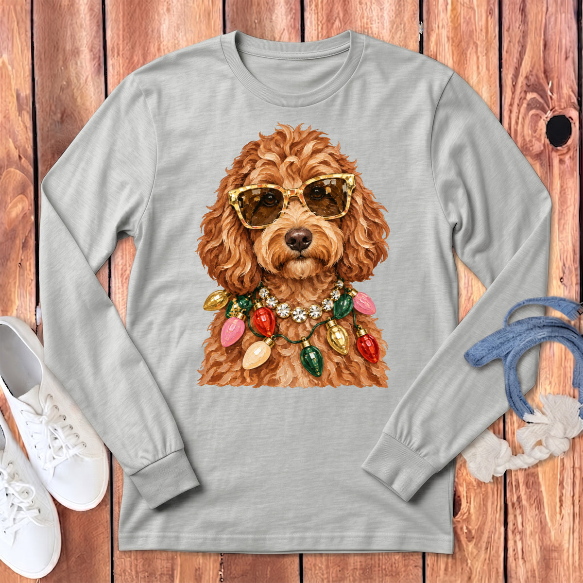 Brown poodle wearing sunglasses and a string of Christmas lights on a gray long-sleeve shirt.