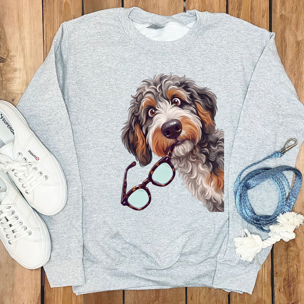 A grey crewneck sweatshirt featuring a graphic of a shaggy dog holding glasses in its mouth, surrounded by white sneakers and a blue leash on a wooden background.
