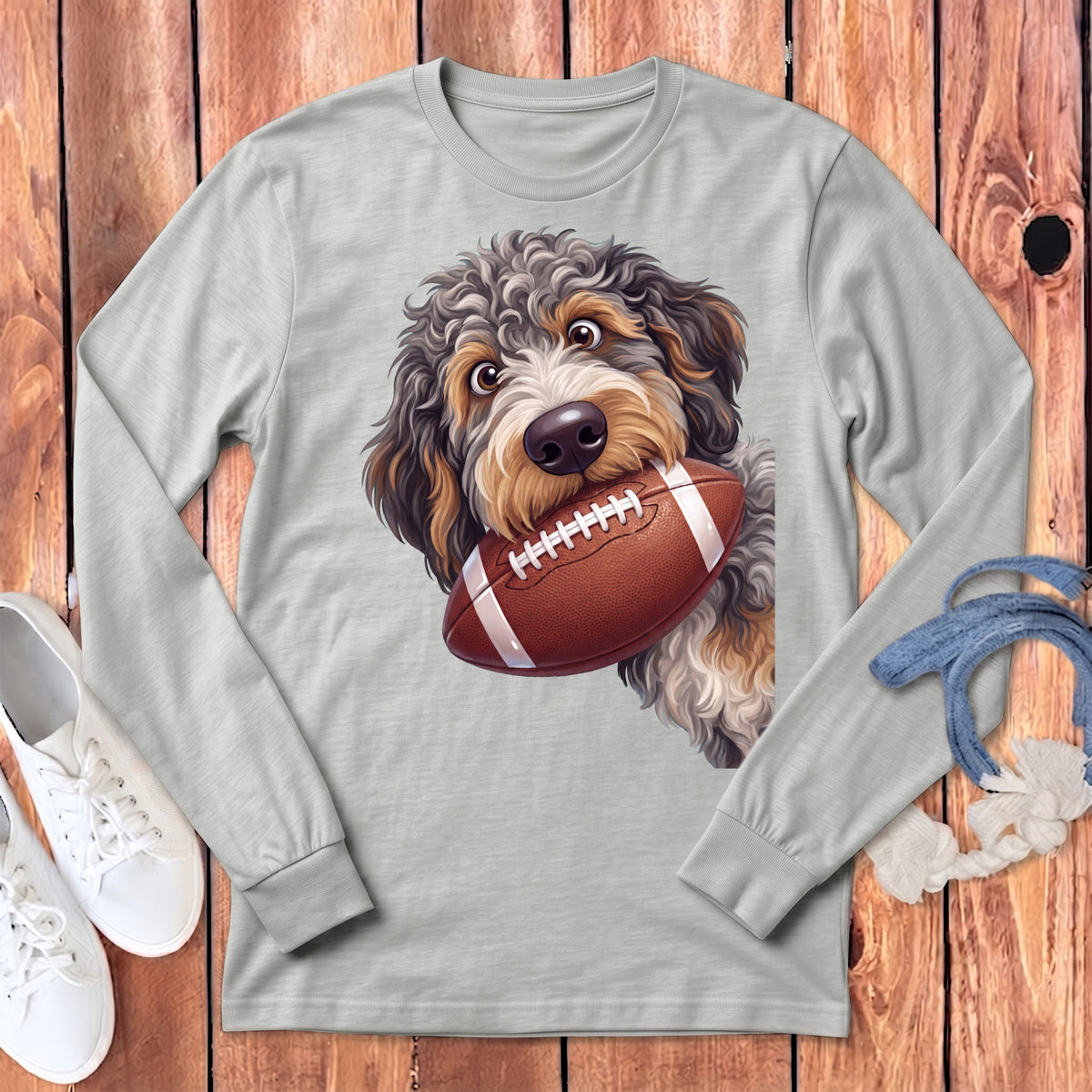 A light grey long-sleeve t-shirt featuring an illustration of a fluffy dog holding a football.