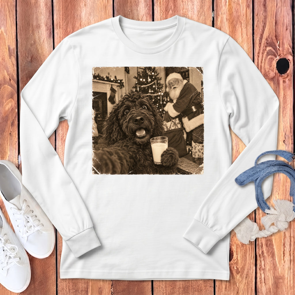 White long-sleeve t-shirt featuring a vintage sepia graphic of a curly dark dog holding a glass of milk with Santa Claus in the background.