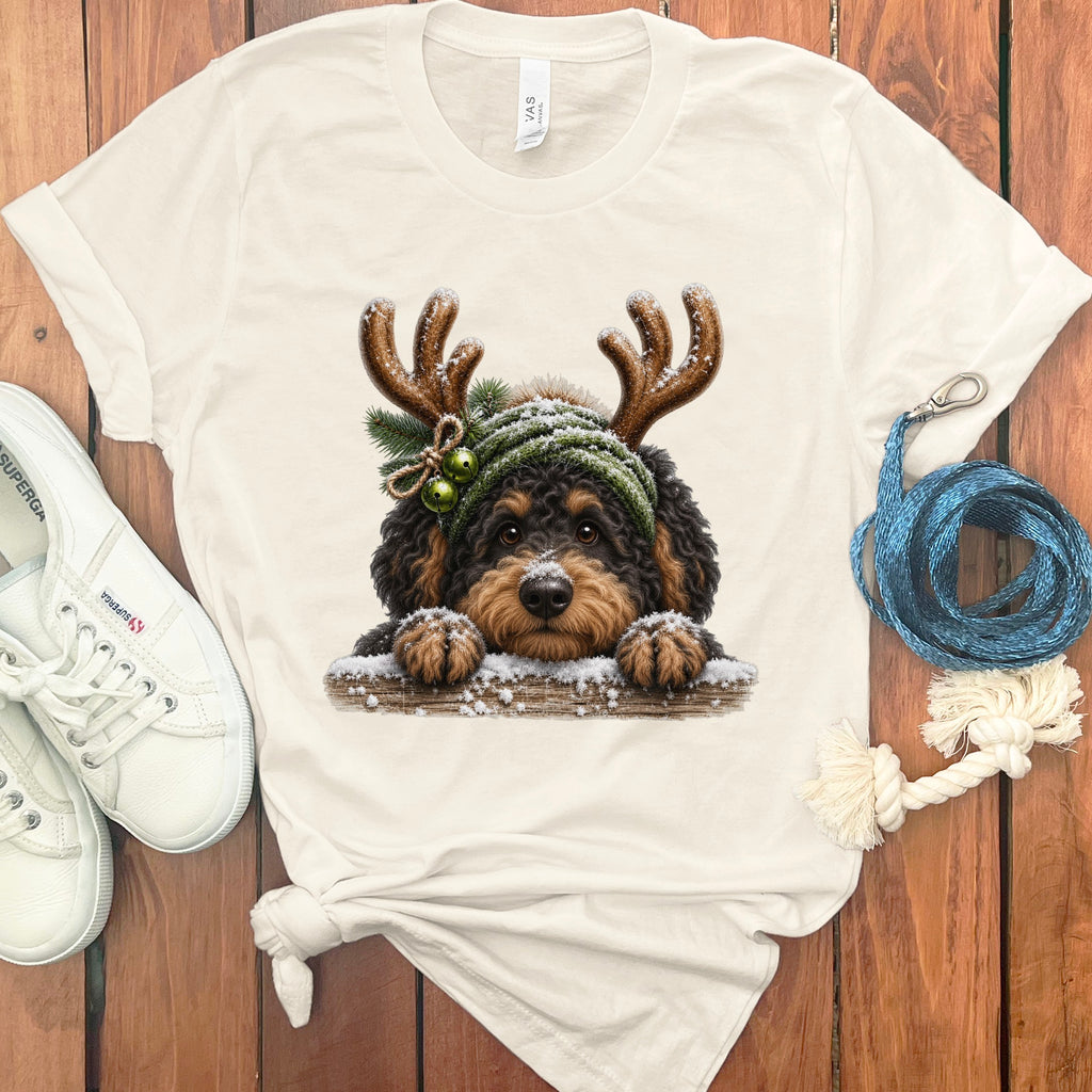 Cream t-shirt featuring a Bernedoodle wearing antlers, winter hat, and bells.