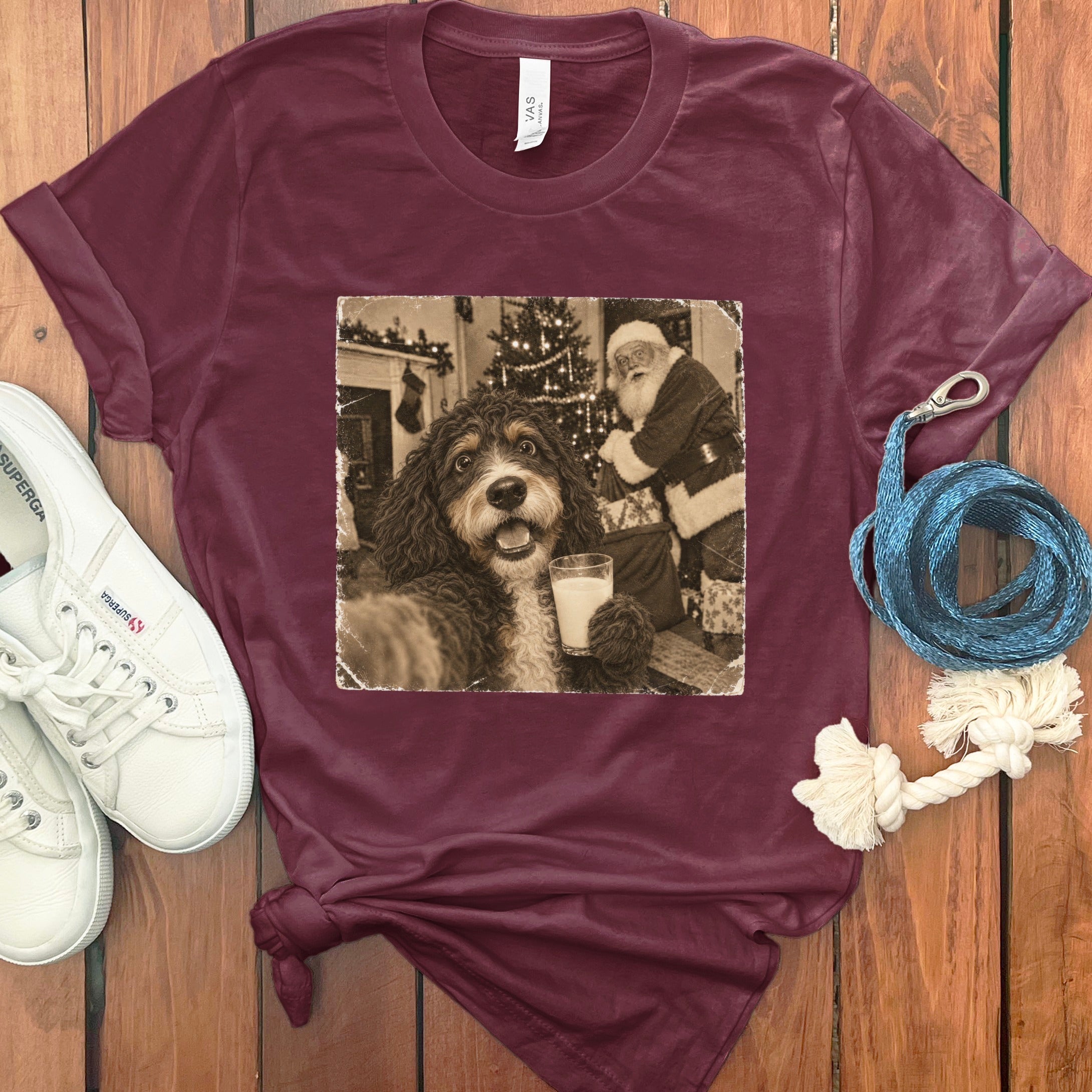 Maroon short-sleeve t-shirt featuring a graphic of a dog holding a glass of milk with Santa Claus in the background.