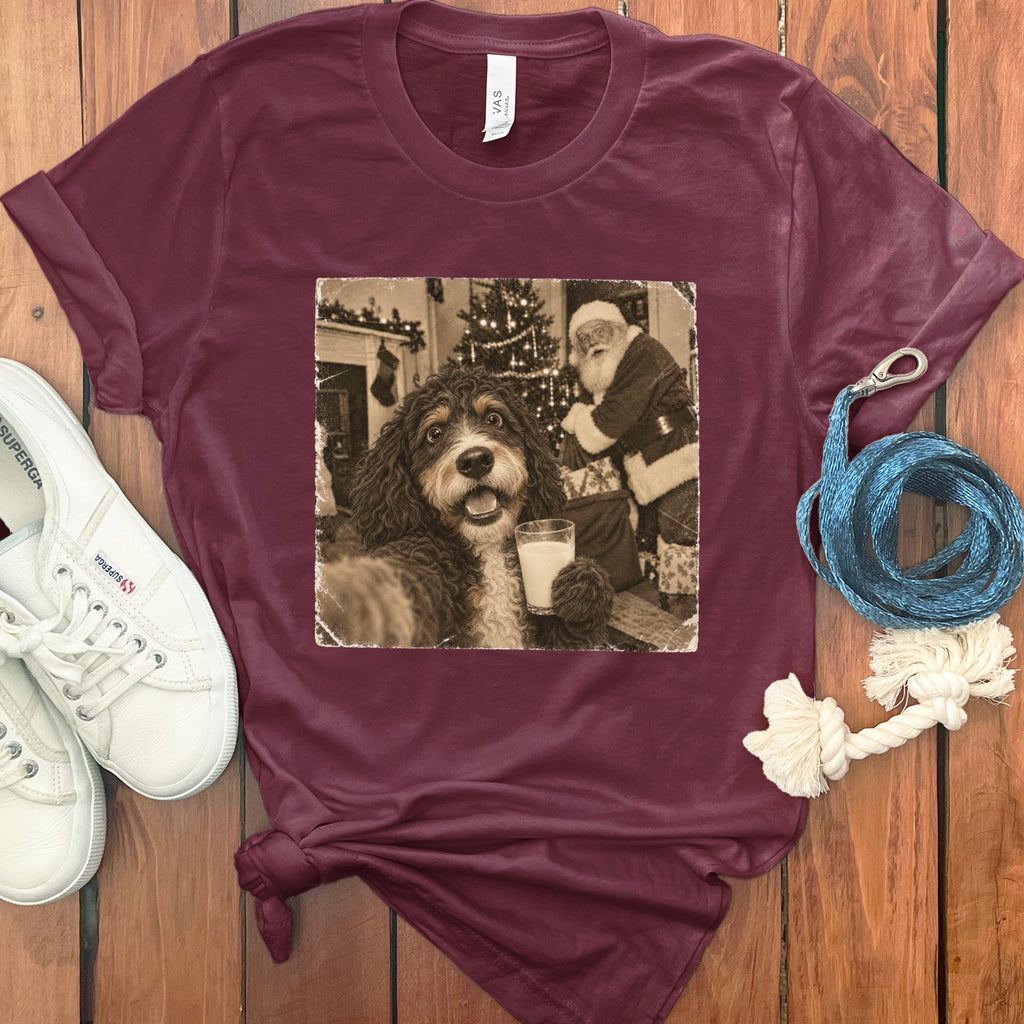 Maroon short-sleeve t-shirt featuring a graphic of a dog holding a glass of milk with Santa Claus in the background.
