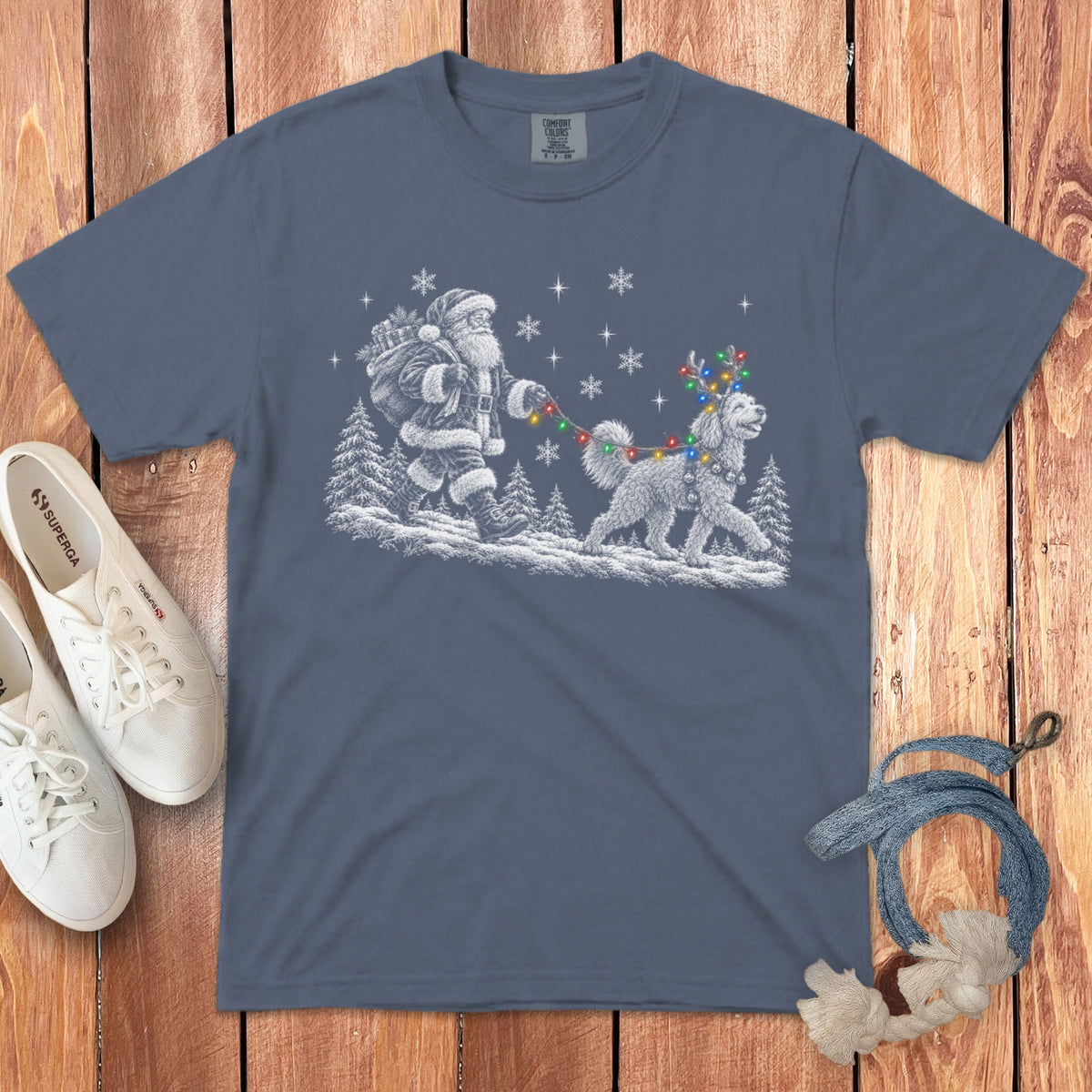 A slate blue t-shirt printed with Santa walking a fluffy dog wearing reindeer antlers and colorful lights.
