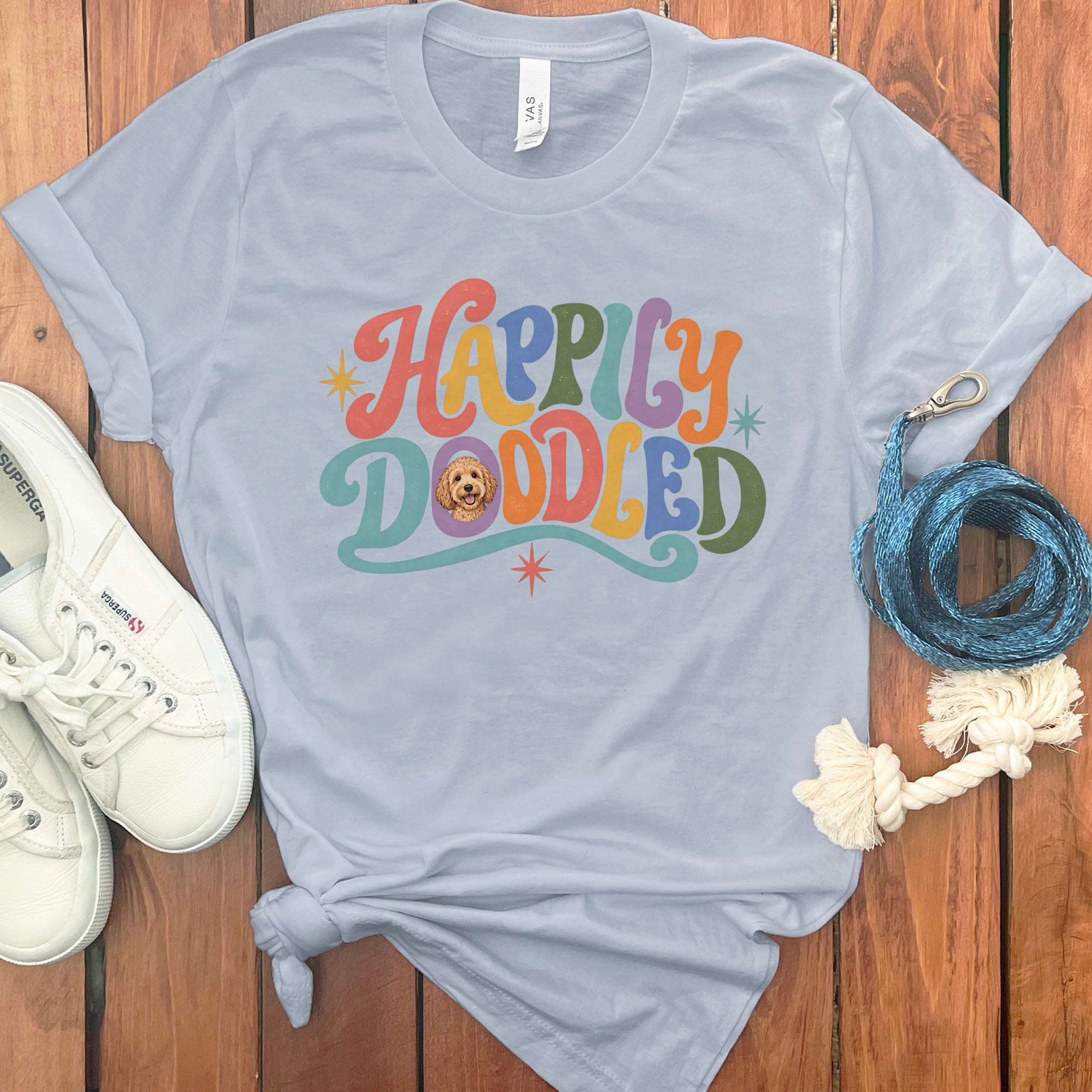 Light blue t-shirt with "Happily Doodled" in colorful retro font and dog graphic.