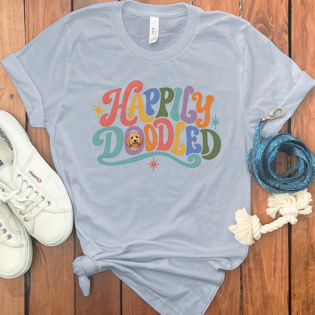 Light blue t-shirt with "Happily Doodled" in colorful retro font and dog graphic.