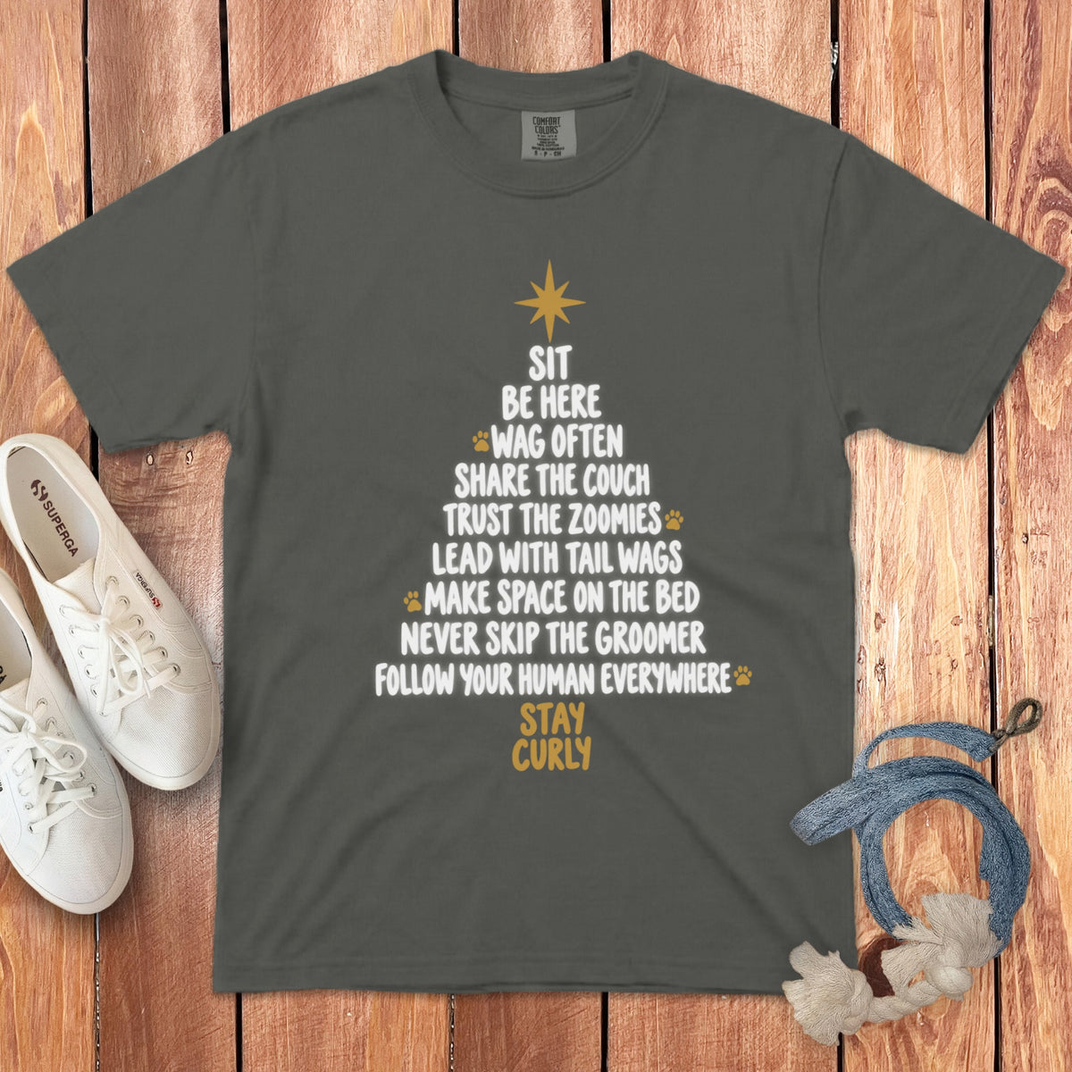 A dark gray t-shirt with a dog-themed Christmas tree graphic, white sneakers, and a rope toy on a wooden background.
