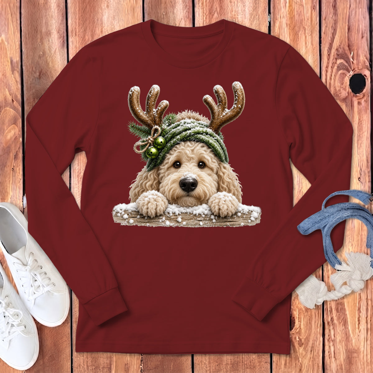 Goldendoodle wearing a green knitted hat with antlers and bells on a maroon shirt.