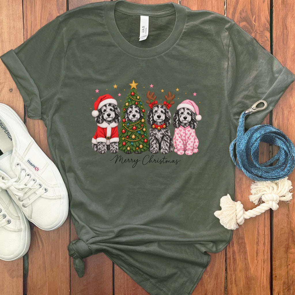 An olive green t-shirt features a Christmas graphic of four dogs, white sneakers, and a leash on a wooden background.