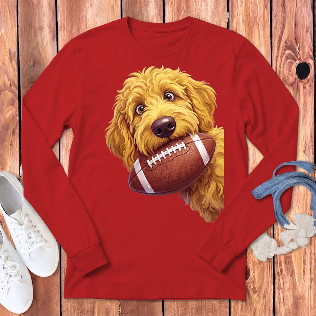 Golden doodle dog holding a football on a red long-sleeve shirt.