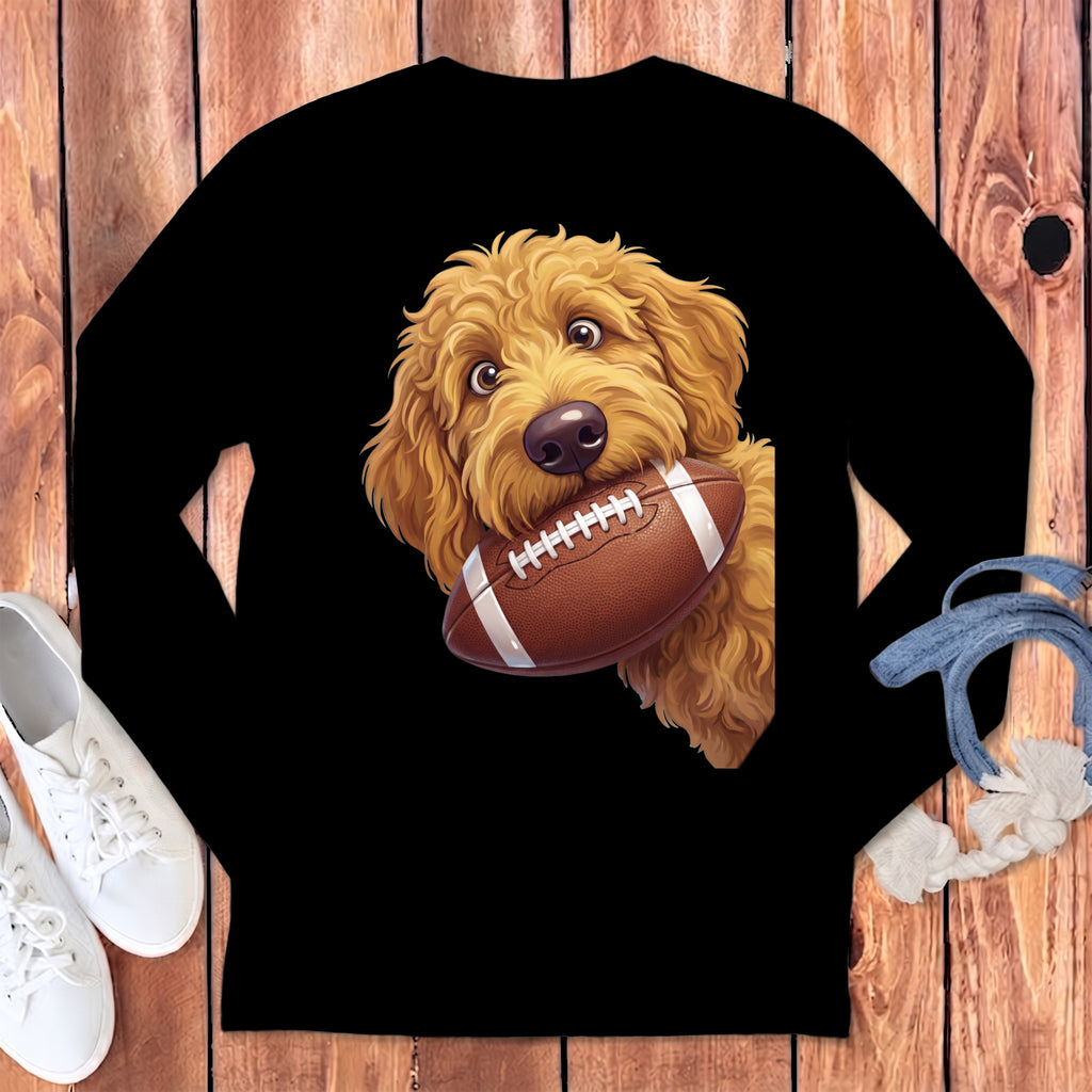 Goldendoodle dog with football in mouth on a black long-sleeve shirt.