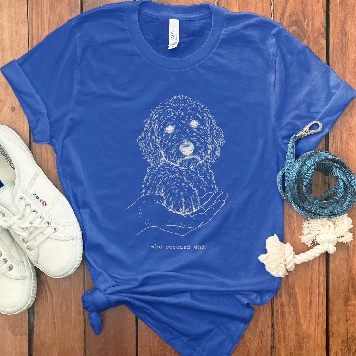 Blue t-shirt with a sketch of a dog's face and paw on a hand, text "who rescued who."