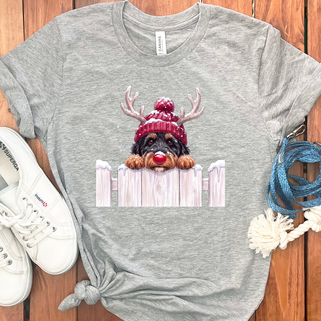 Grey t-shirt with a dog wearing a red beanie and antlers peeking over a fence.