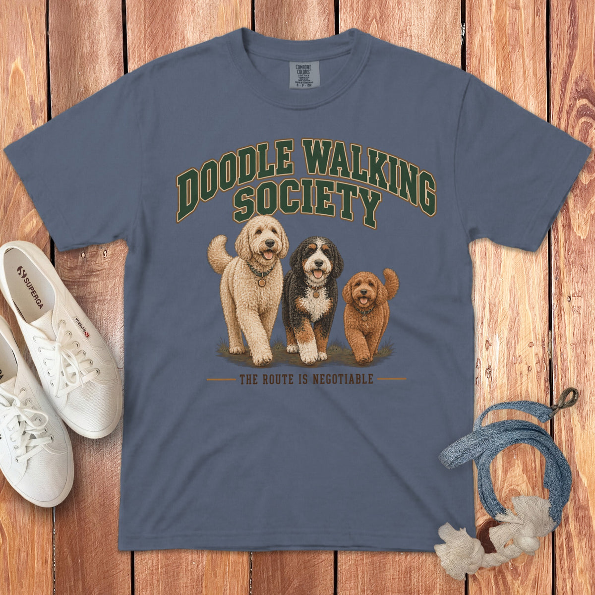 Blue crewneck t-shirt with Doodle Walking Society graphic, three doodle dogs, and text on wooden background.