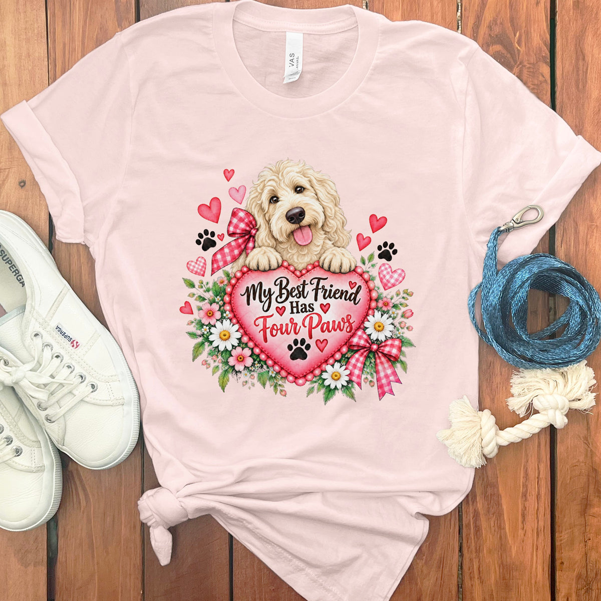 Light pink t-shirt featuring a Golden Doodle graphic, text reading My Best Friend Has Four Paws, white sneakers, and a blue leash on a wooden background.