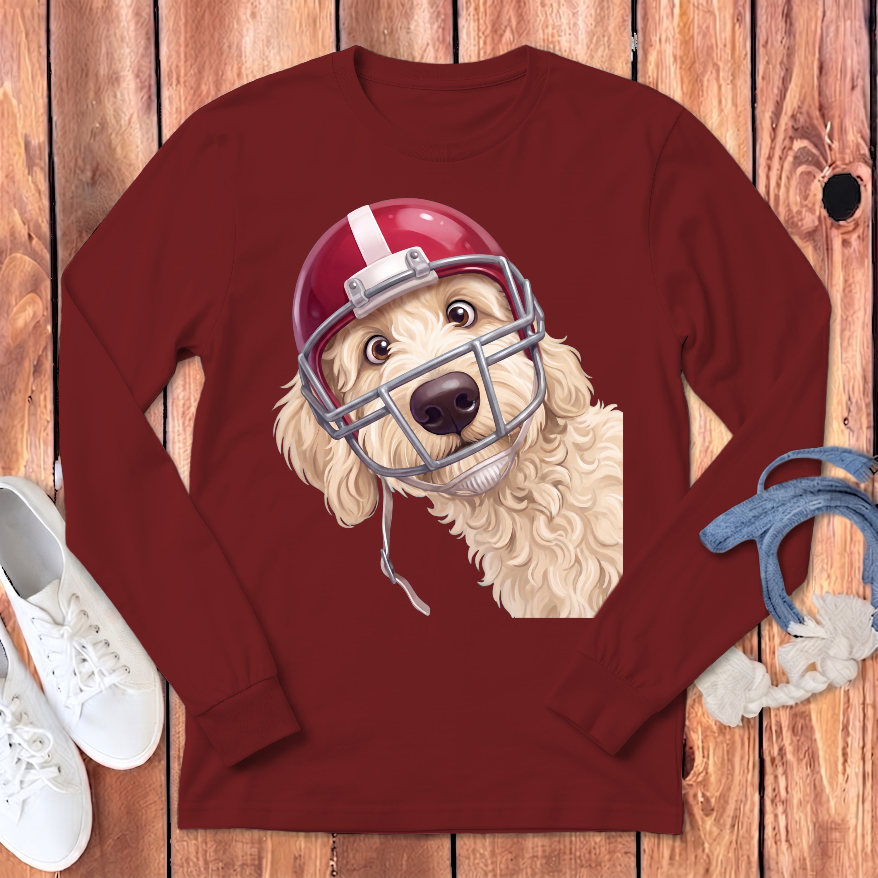 Cream-colored dog wearing a red and white football helmet peeking from a maroon long-sleeve shirt.