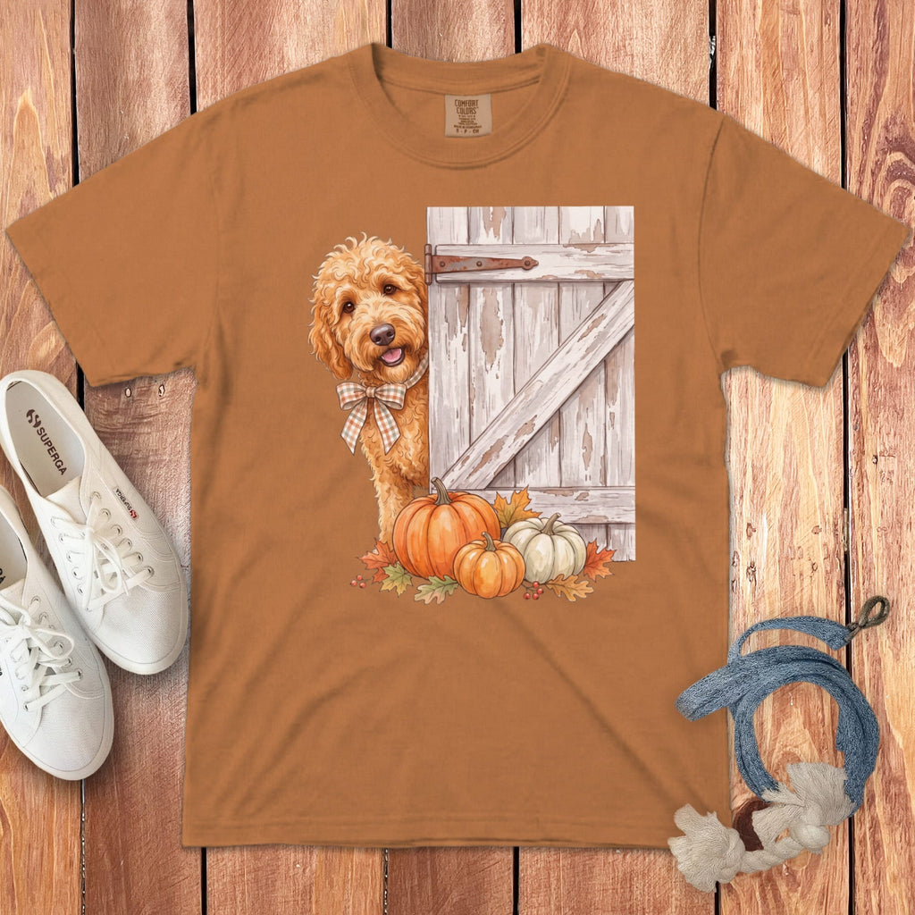 Brown t-shirt with doodle dog peeking from behind a rustic barn door and pumpkins.
