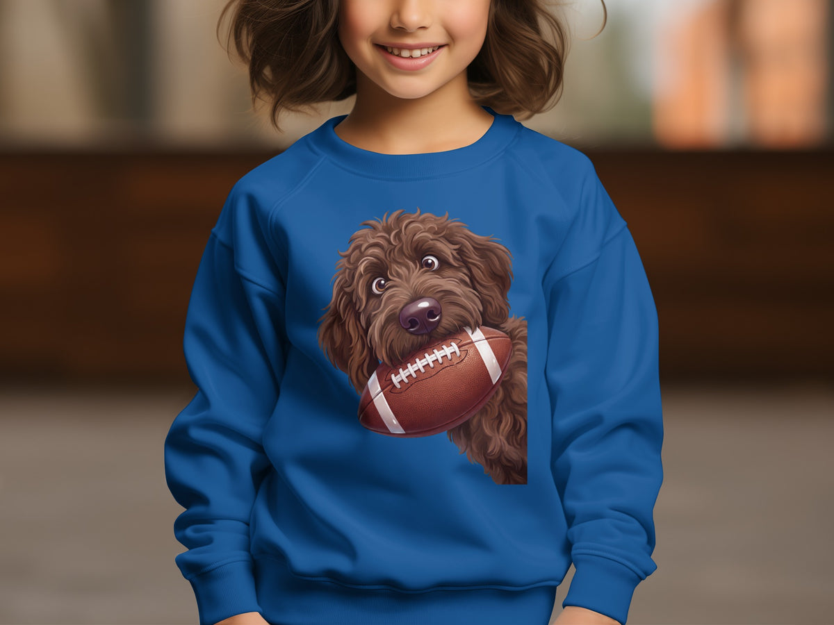 Brown doodle dog holding a football on a royal blue sweatshirt.