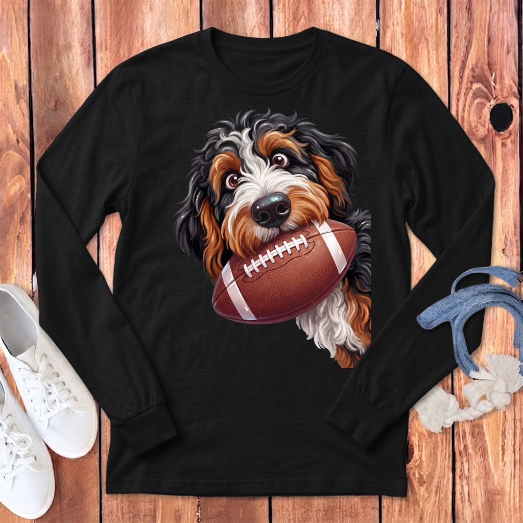 Bernese Mountain Dog holding an American football in its mouth on a black long-sleeved shirt.
