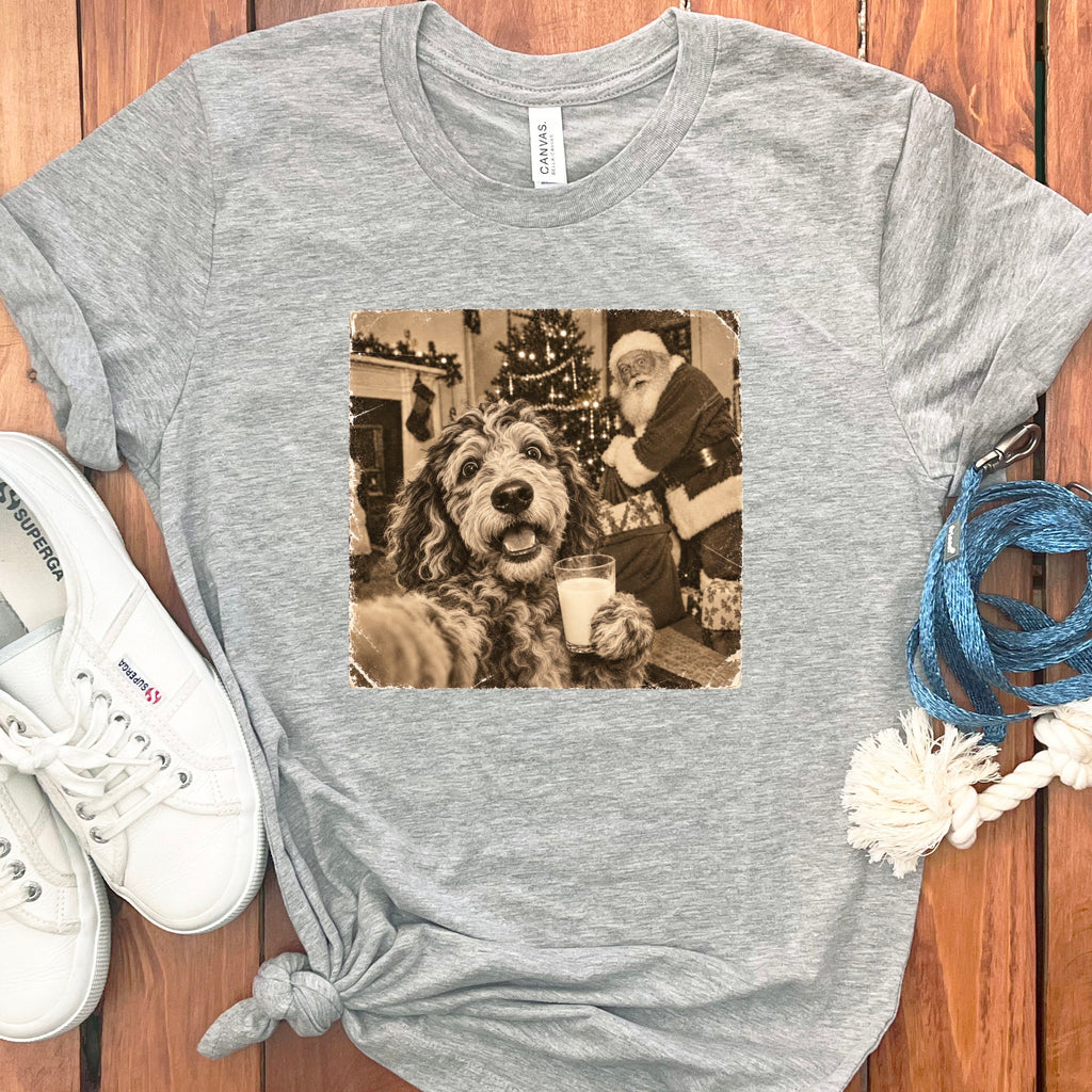 A heather gray t-shirt features a vintage graphic of a fluffy dog holding a glass of milk with Santa Claus in the background.