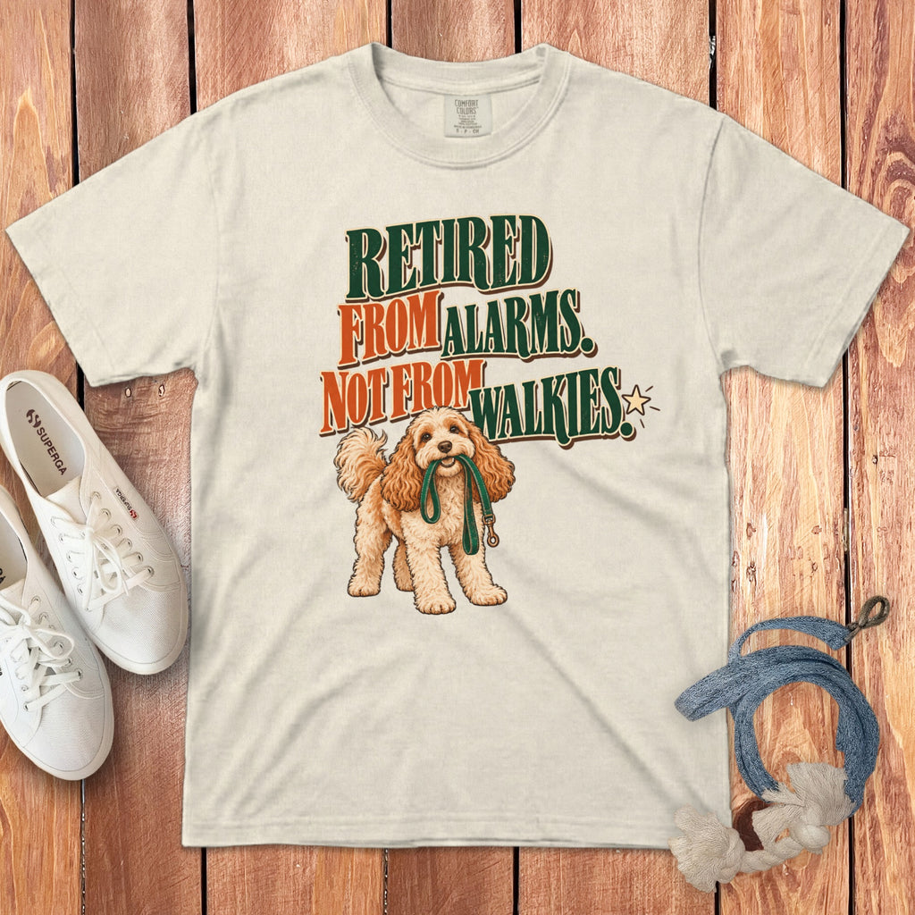 Off-white t-shirt featuring a graphic of a golden doodle dog holding a leash and text reading Retired From Alarms Not From Walkies.