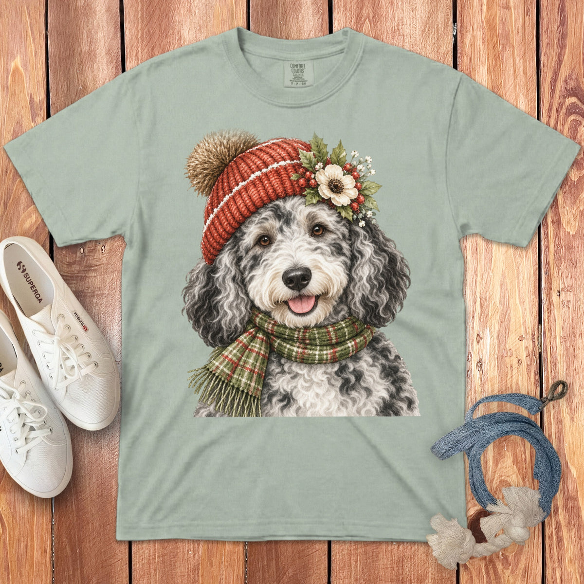 Light green t-shirt with watercolor art of a dog wearing a festive hat and scarf.