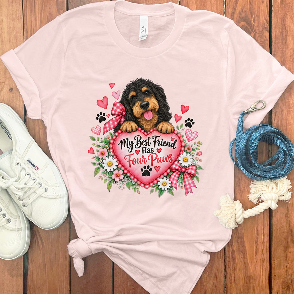 Light pink t-shirt featuring a cartoon dog holding a heart with the text My Best Friend Has Four Paws, surrounded by flowers, hearts, and paw prints.